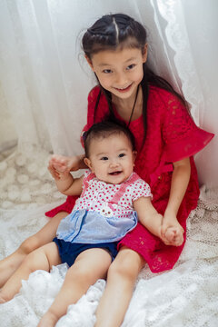 An Asian girl playing indoors with her baby.