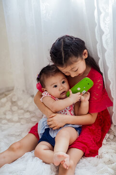 An Asian girl playing indoors with her baby.