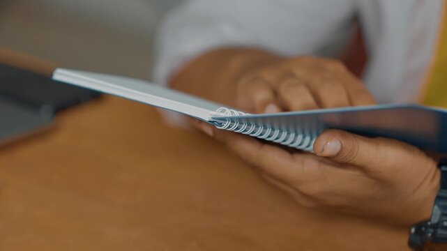 Close-up of warm light illuminating male hands turning book page, nestled atop stacked volumes in soft, muted library setting, creating intimate reading environment, selective focus, slow motion.