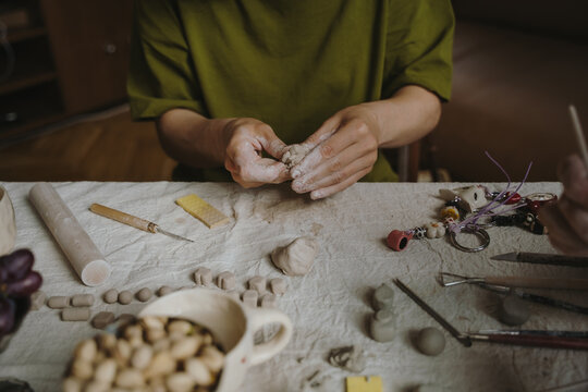 Female hands shaping clay with pottery tools in home studio.