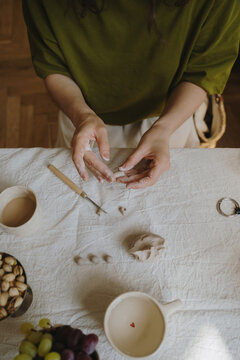 Female hands shaping clay with pottery tools in home studio.