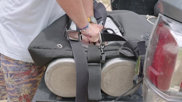 Male diver preparing his scuba gear, adjusting straps on the double tank rig on a pickup truck