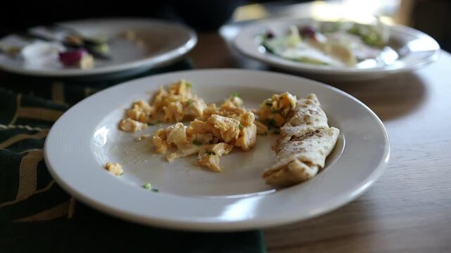 Close up view of freshly cooked scrambled eggs served on a white plate with pieces of toasted flatbread. The scene is set on a wooden dining table during a cozy morning routine, capturing ideas of