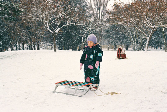 A little girl with a sled near an ice sledding hill.