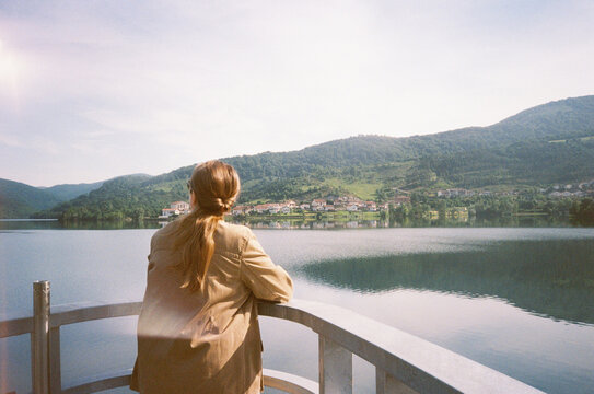Rear View Of Woman Admiring Scenic Lake And Village Mountain 
