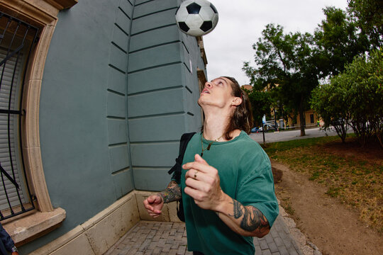 Young man practices soccer skills with a ball near a building