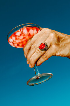 in a tight crop, a man holds a glass of red cocktail and ice