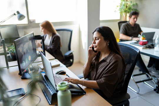 Businesswoman multitasking on laptop taking phone call