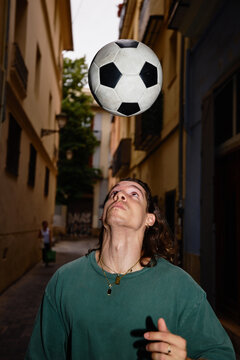 Man juggles soccer ball in narrow street during afternoon