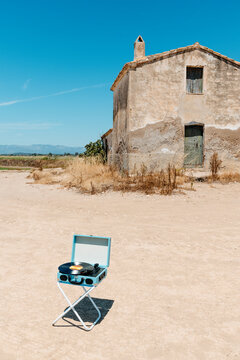 an old rural farmhouse rises above a portable record player on a stool