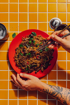 Person eating beef stir fry noodles with chopsticks 