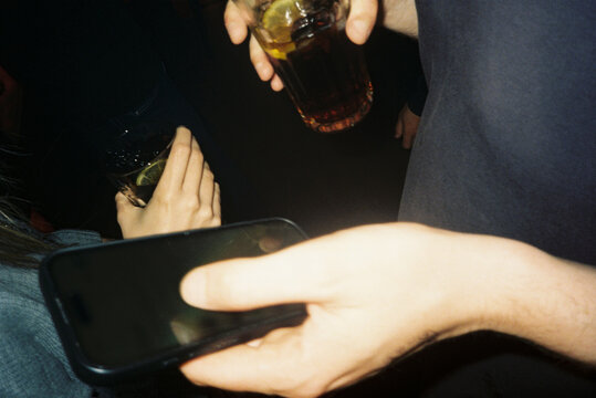 Hands Hold Drinks and a Phone in Night Club