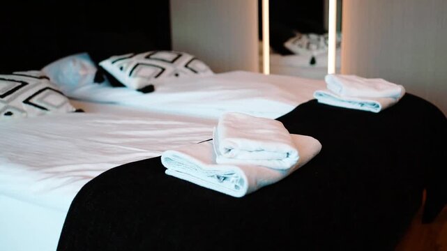Close up view of a neatly made bed featuring soft white sheets, pillows, and decorative throw pillows with a black and white geometric square pattern. The scene captures modern bedroom interior design