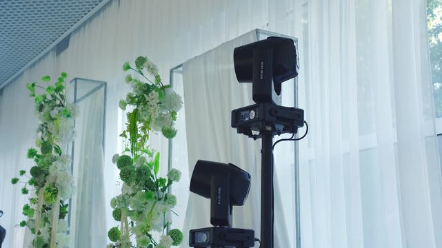 Spotlights in the corner of the banquet hall against the backdrop of a flower-decorated wedding arch. Moving beams on stands during the event's disco. Festive atmosphere and lighting equipment.