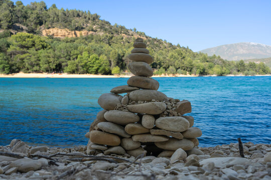 Sainte-Croix-du-Verdon, France - 07 05 2026: Detail view of the Lake Sainte-Croix, Cairn made of stones and pebbles, beach, hills and forests in sunny blue sky