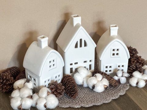 Minimalist white ceramic village houses styled with cotton bolls and pinecones in a neutral palette, creating a cozy Scandinavian display for autumn, winter, Thanksgiving and Christmas.