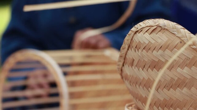 Close-up of an elderly Thai artisan skillfully weaving a handmade bamboo basket using traditional techniques in a rural village of Northern Thailand. The image highlights sustainable craftsmanship, na