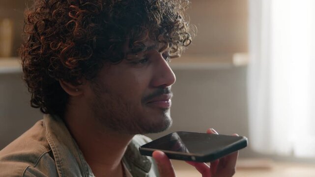 Close up Indian man recording voice message on smartphone at home kitchen speaking on speakerphone friendly Arabian male dictating audio voicemail talking with friend using mobile communication app
