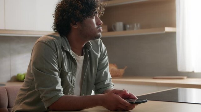 Unhappy Indian Arabian man using smartphone at home kitchen stressed exhausted tired ethnic male reading bad news disappointed mobile phone lost connection frustrated guy scrolling cellphone indoor