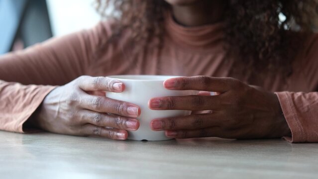 Women's hands hold a mug of hot tea in the morning during the cold season. A young woman warms her hands on a very hot cup of tea.
