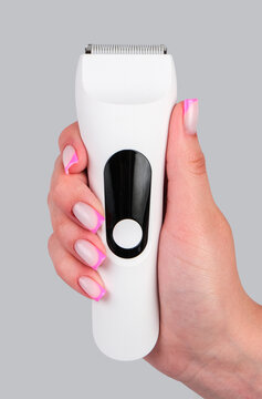 A close-up shot of a person holding a sleek white waterproof electric beard trimmer with water droplets, isolated against a solid clean grey background.