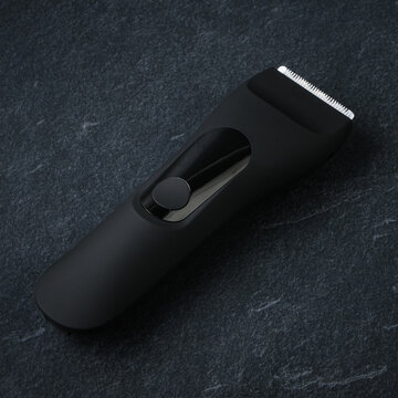 High-quality product photography of a sleek black cordless electric hair clipper and trimmer, placed on a premium dark slate stone texture background with shadow.