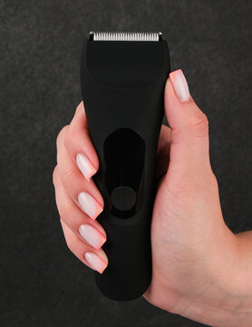Close-up product photography of a premium black waterproof electric hair clipper and beard trimmer covered in water drops, held in a hand on a grey background.
