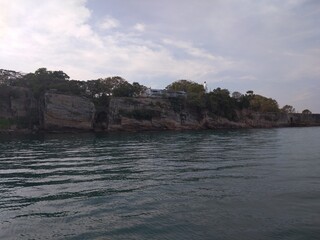Fototapeta premium Calm sea against rocky coastline with trees under cloudy sky