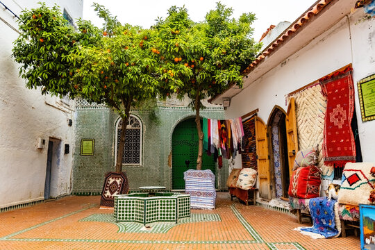Traditional Moroccan courtyard with vibrant mosaic tiles, orange trees, handcrafted Berber rugs and souvenir shops in the heart of Chefchaouen, the famous Blue City in northern Morocco