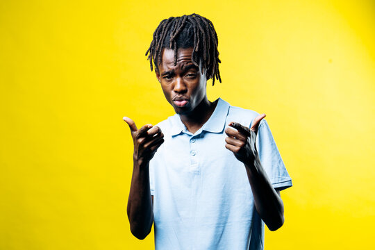 Young black man with dreadlocks and confident expression pointing fingers on a vibrant yellow studio background