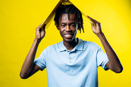 Young man with dreadlocks smiling, holding a yellow folder over his head like a roof, representing security and protection