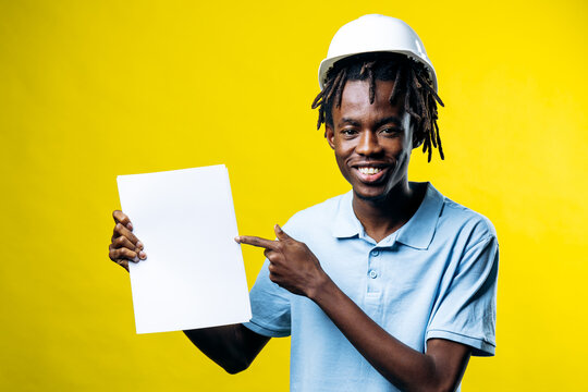 Confident young black man engineer wearing hard hat holding empty paper and pointing, presenting new project or plan