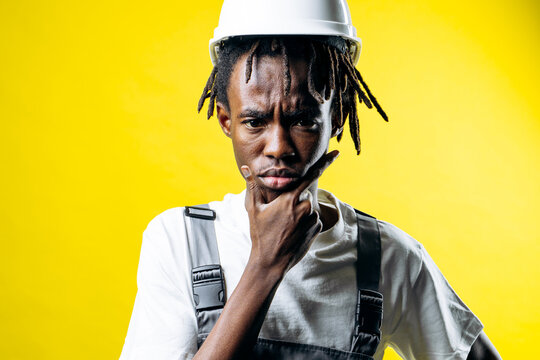 African construction worker wearing a hard hat and overalls, contemplating new design ideas on a bright yellow background