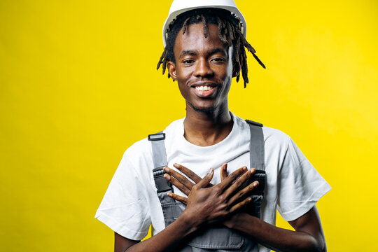 Young man wearing a hard hat and overalls, expressing gratitude and professionalism against a vibrant yellow background