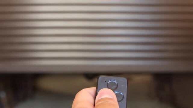 Hand pressing remote control button to open an automated garage door with a vintage 1970s motorcycle standing in the background ready for a ride