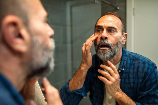Middle-aged man examining wrinkles in bathroom mirror