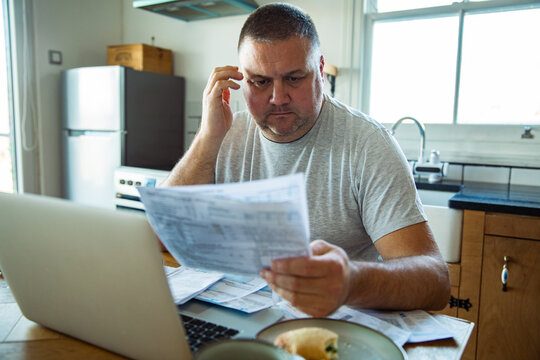 Concerned man reviewing household bills at kitchen table