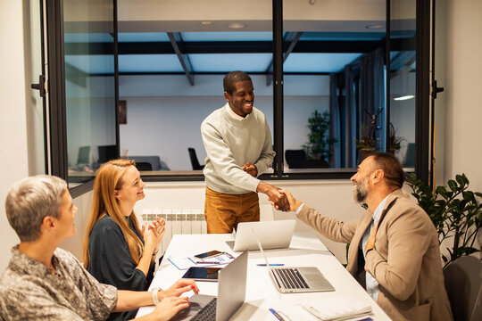Coworkers shaking hands during team meeting in modern office