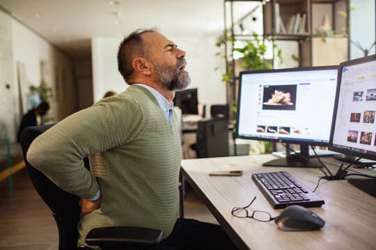 Middle-aged man experiencing lower back pain at office desk