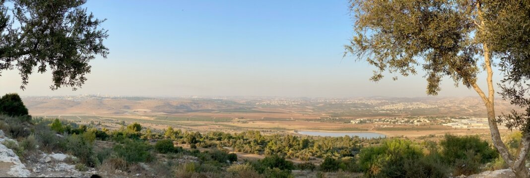 Panoramic view over the Ayalon Valley from Canada Park in Israel. Scenic landscape with rolling hills, trees and open countryside under a clear blue sky