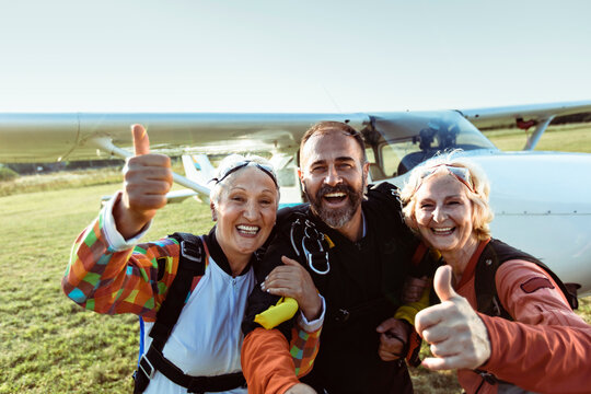 Happy senior friends with skydiving gear at airfield