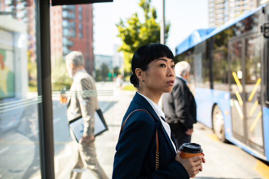 Businesswoman waiting for bus at city bus stop with coffee