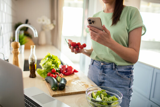Young woman checking recipe on phone while making fresh salad in a home kitchen