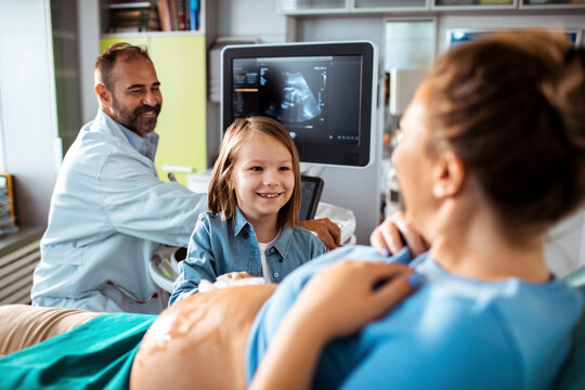 Obstetrician performing prenatal ultrasound while sibling watches in clinic