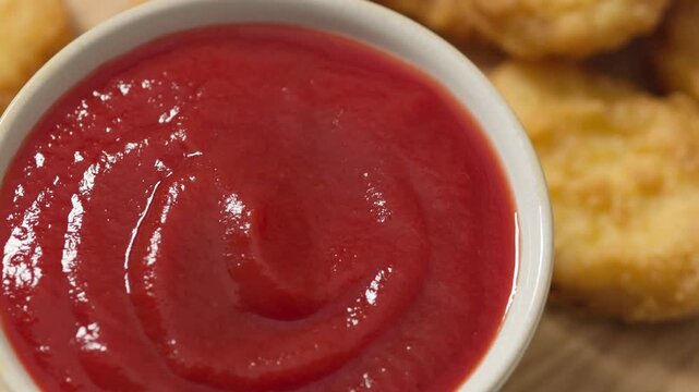 Top view of crispy fried chicken nuggets served with a bowl of tomato ketchup on a rustic wooden board. 