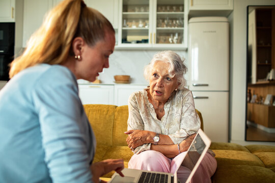 Caregiver helping senior woman with laptop at home