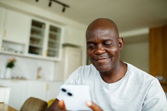 Smiling mature man using smartphone in home kitchen