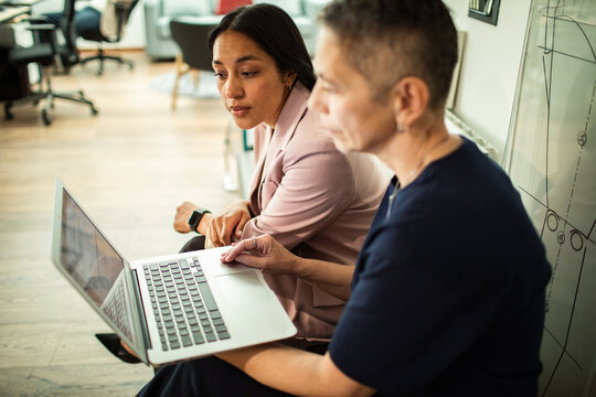 Two businesswomen collaborating on laptop in modern office