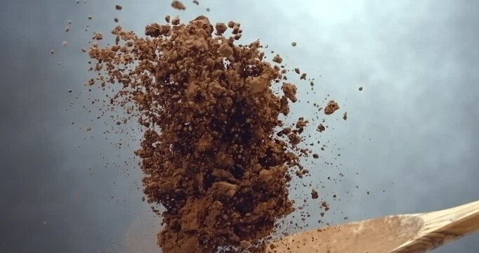 Cocoa powder falling from wooden spoon chocolate dust cloud slow motion