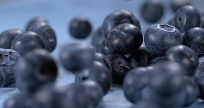 Fresh blueberries fall and bounce across a blue surface in slow motion